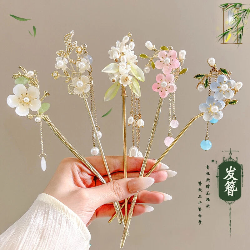 Gold-tone flower hairpins with pearls and dangling tassels, held in hand
