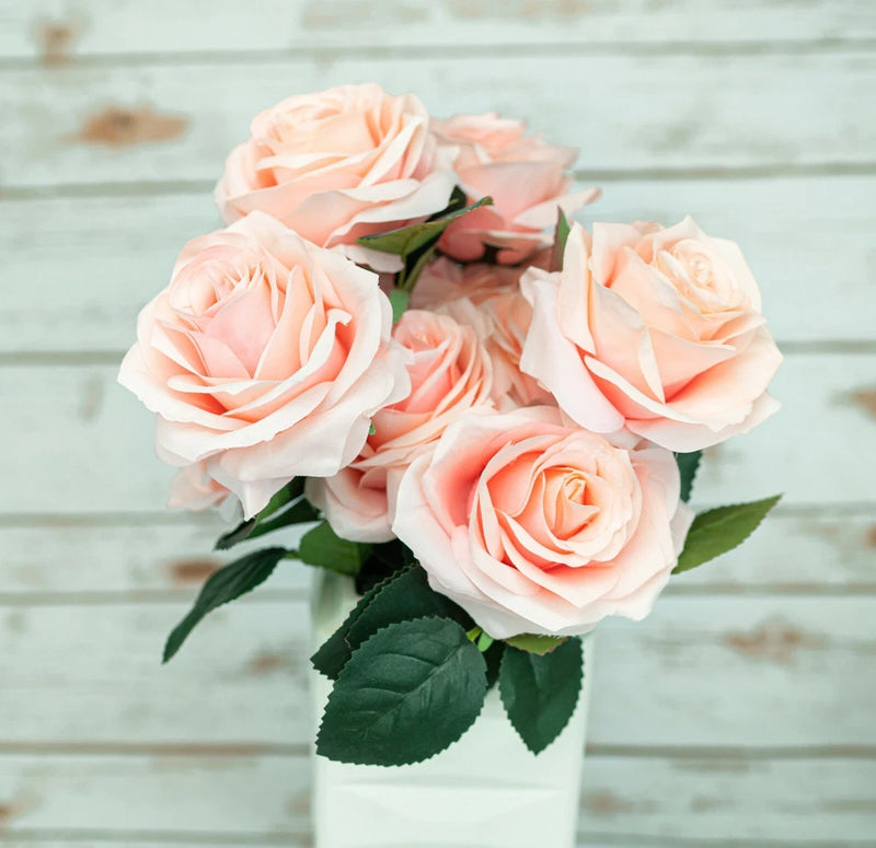 Artificial rose bouquet with five peach-pink silk roses and green leaves in a white vase