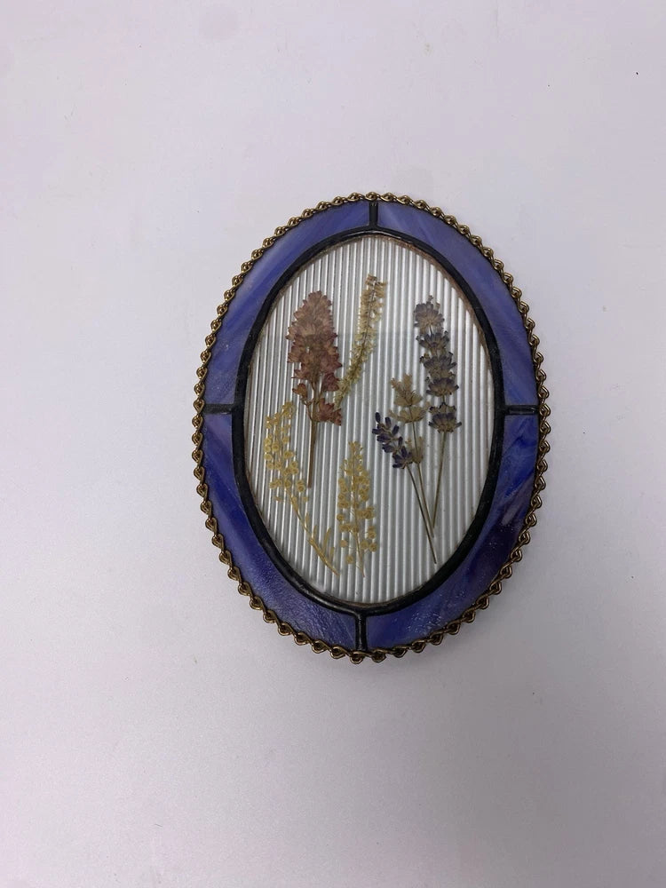Oval glass floral wall plaque with blue backing, gold beaded frame, dried stems inside
