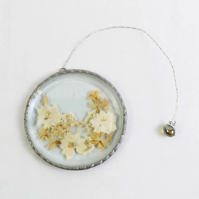 Hanging glass flower medallion with pressed dried blooms, silver frame and loop.