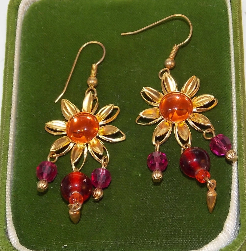 Gold-tone sunflower dangle earrings with orange center and pink crystal bead drops.