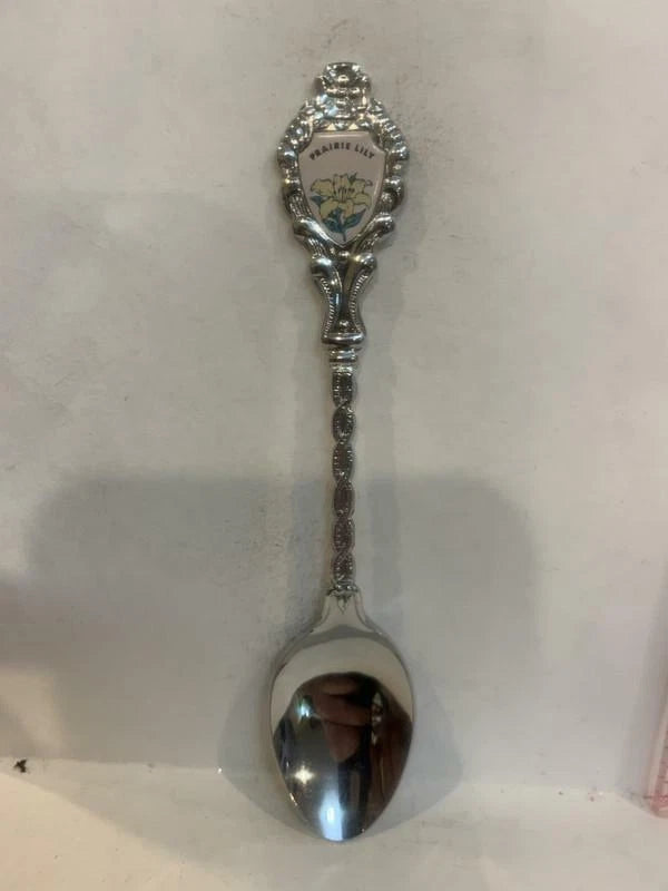 Silver-toned souvenir spoon with ornate handle and lily flower emblem at the top
