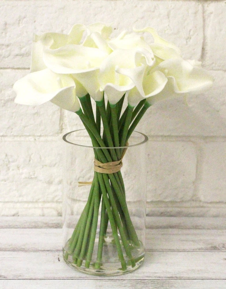 Cream faux calla lily bouquet in clear glass vase with tied green stems
