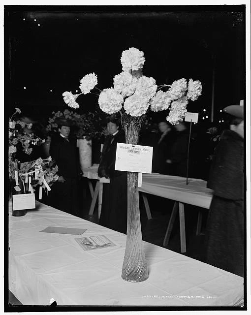 White carnation bouquet in clear glass vase on table with name card