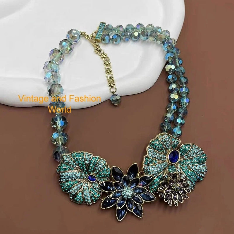 Asymmetrical rhinestone floral necklace with teal leaf pendants and blue crystal accents, gold chain