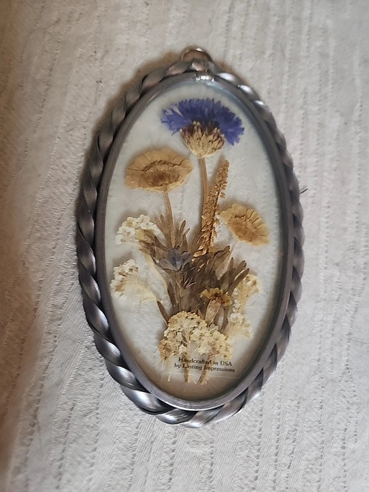 Oval glass pendant with pressed flowers: blue, tan, and beige blooms in metal frame