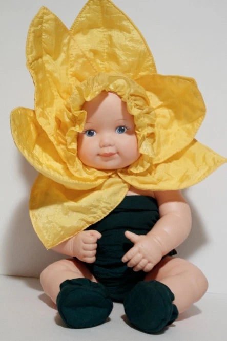 Sunflower-themed baby doll with yellow petal hat and dark green outfit, sitting