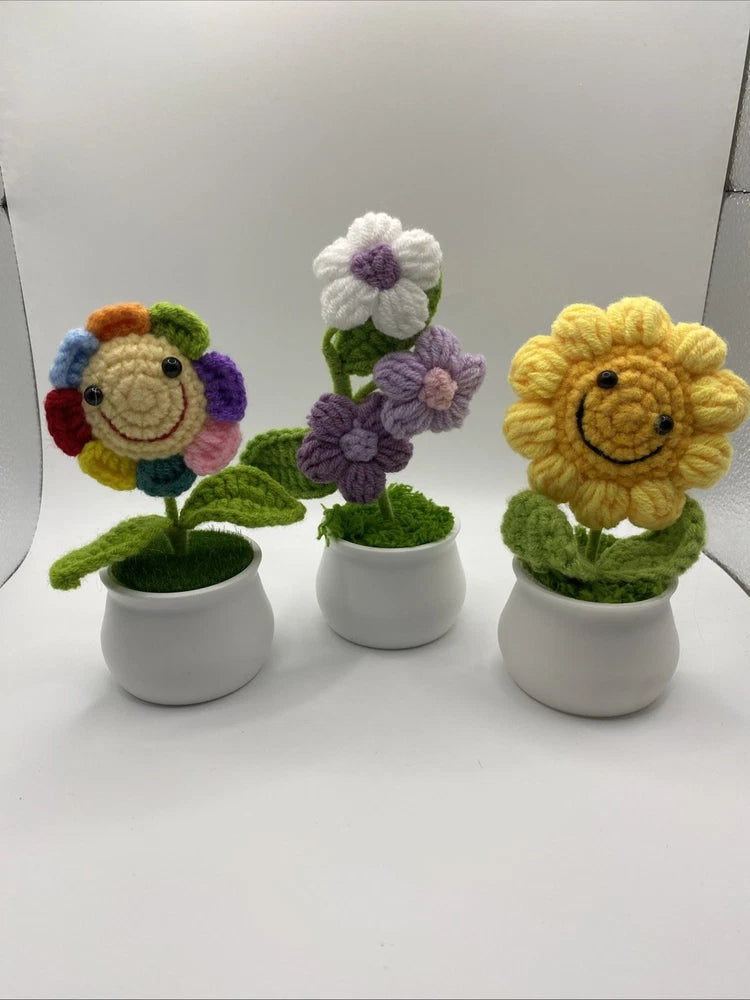 Crochet flower set in three pots: purple, pink, and yellow smiling blooms on green leaves