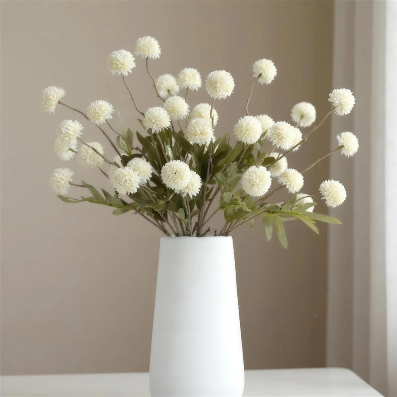 Artificial mum flower bouquet with white blooms and green leaves in a white vase
