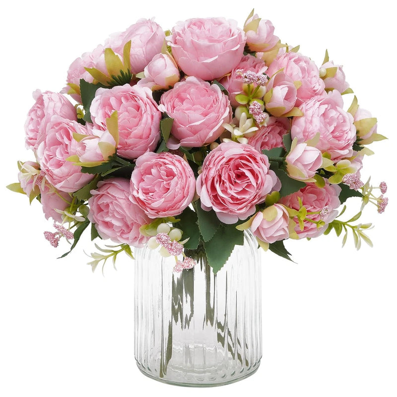 Artificial peony bouquet with light pink blooms in clear glass vase with greenery