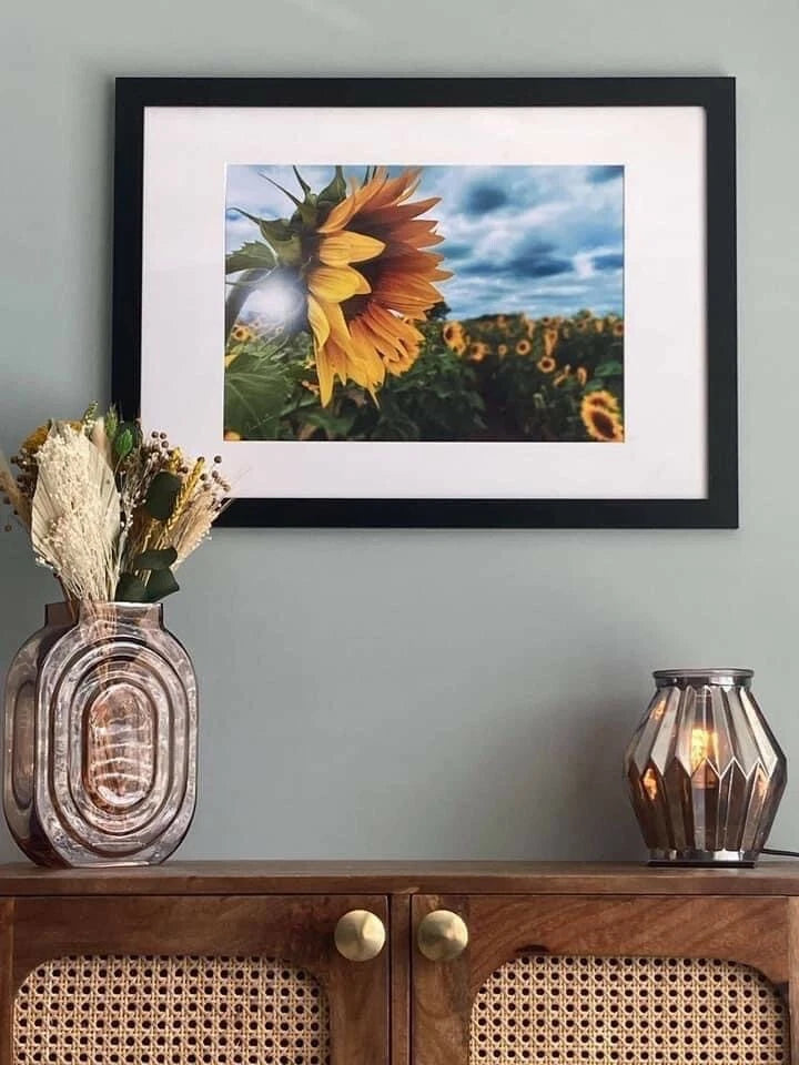 Framed sunflower print with a black frame and white mat, showing a large yellow sunflower