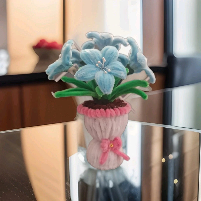 Light blue chenille lily flowers with green leaves in a pink fabric pot