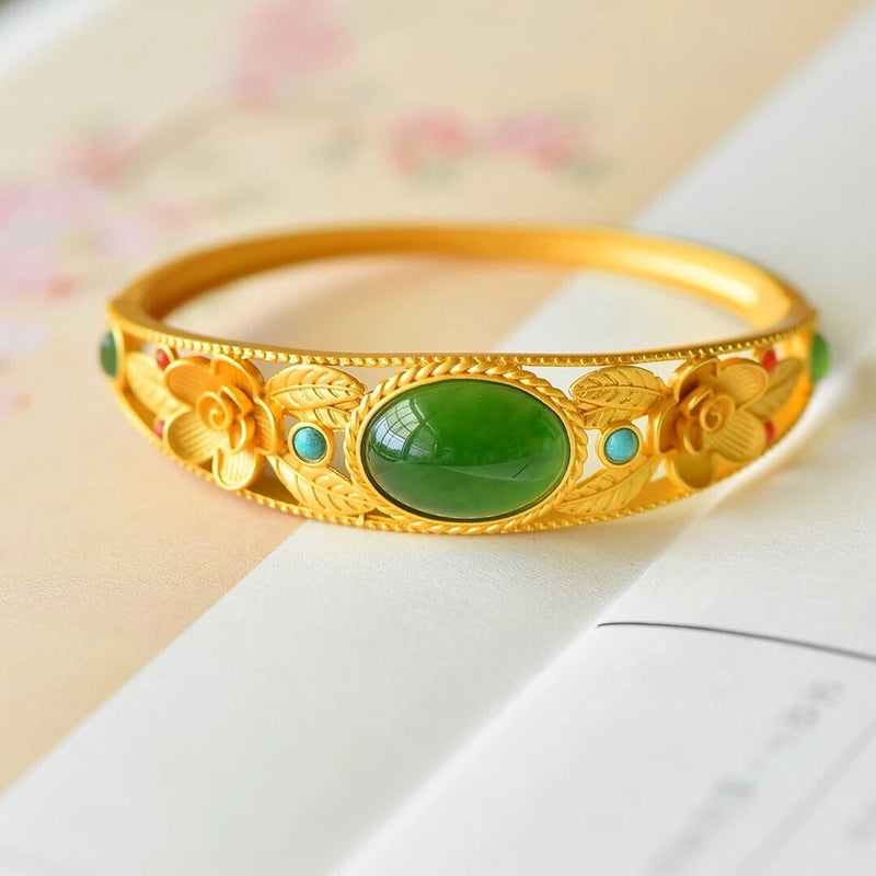 Gold-tone peony bangle bracelet with oval green gemstone and blue accents, engraved frame