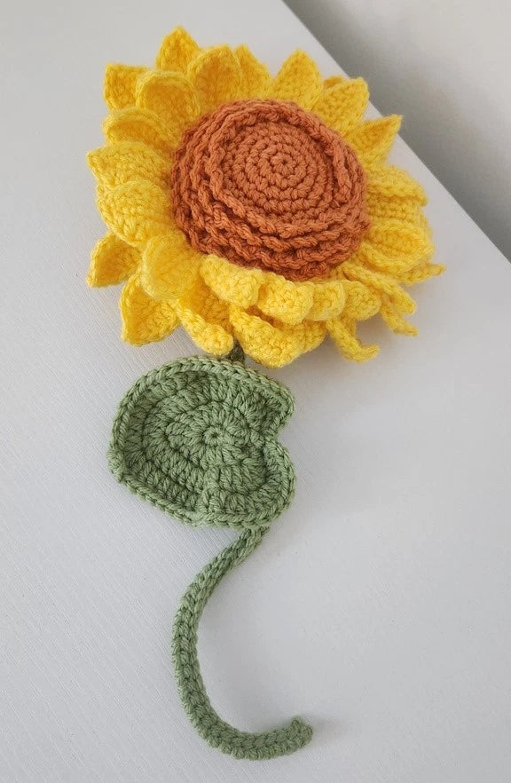 Hand-crocheted sunflower with yellow petals, brown center, green stem and leaf