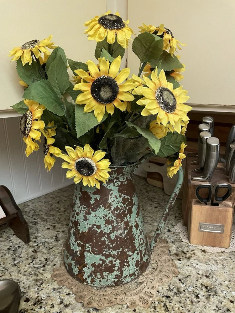 Speckled green ceramic pitcher with bright yellow sunflower arrangement and dark centers.