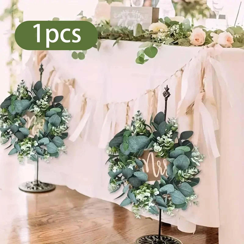 Artificial eucalyptus wreath with green leaves and small white flowers, on metal stand
