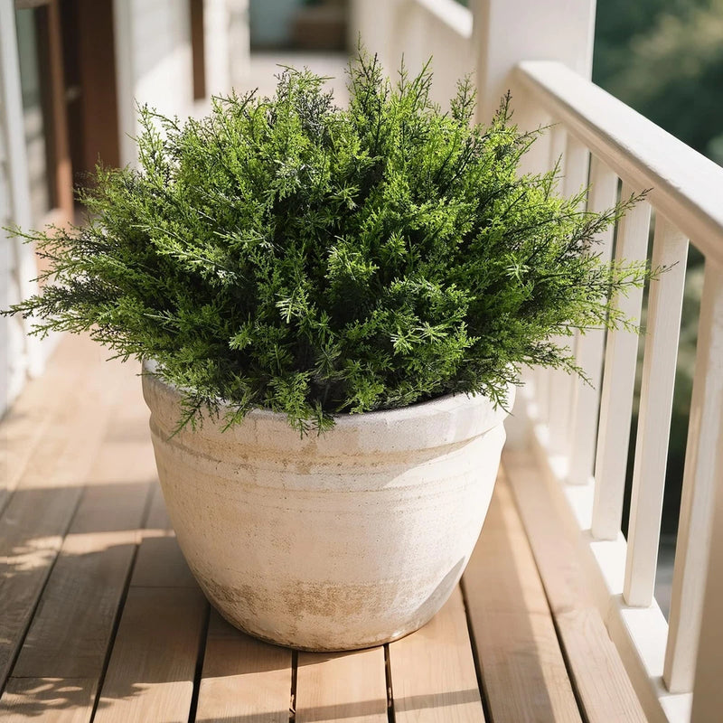 Artificial green leafy plant in large round concrete pot for outdoor decor