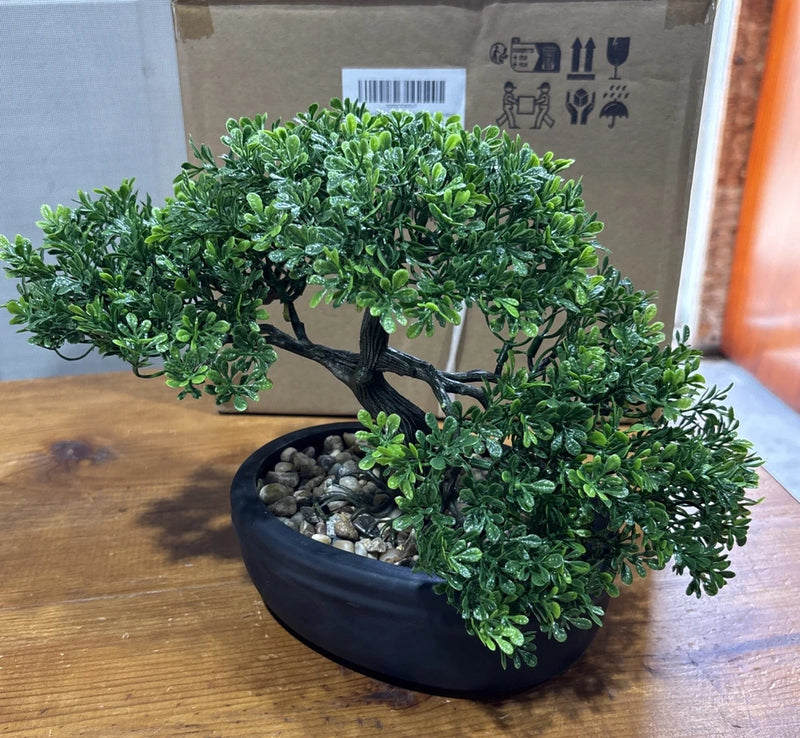 Artificial bonsai tree with green faux foliage and textured trunk in dark oval pot with stones