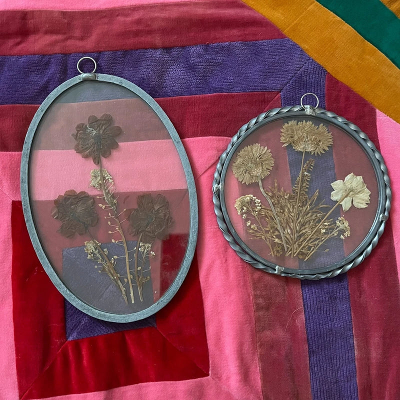 Two framed oval and round glass suncatchers with pressed dried flowers in metal rings.