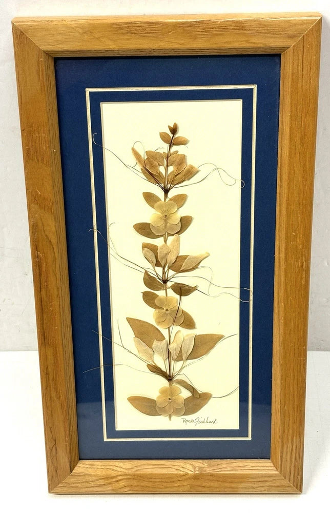 Wooden frame with glass panel holding dried pressed flower stems on a light backing