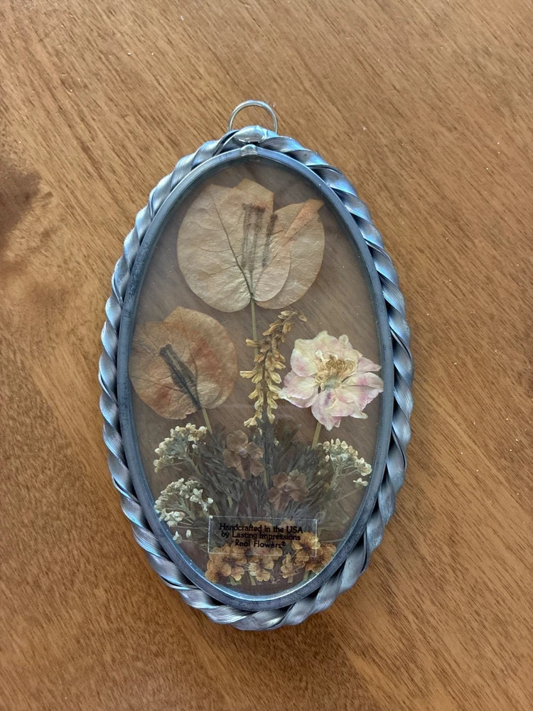 Vintage oval glass frame with pressed dried flowers and botanical stems inside