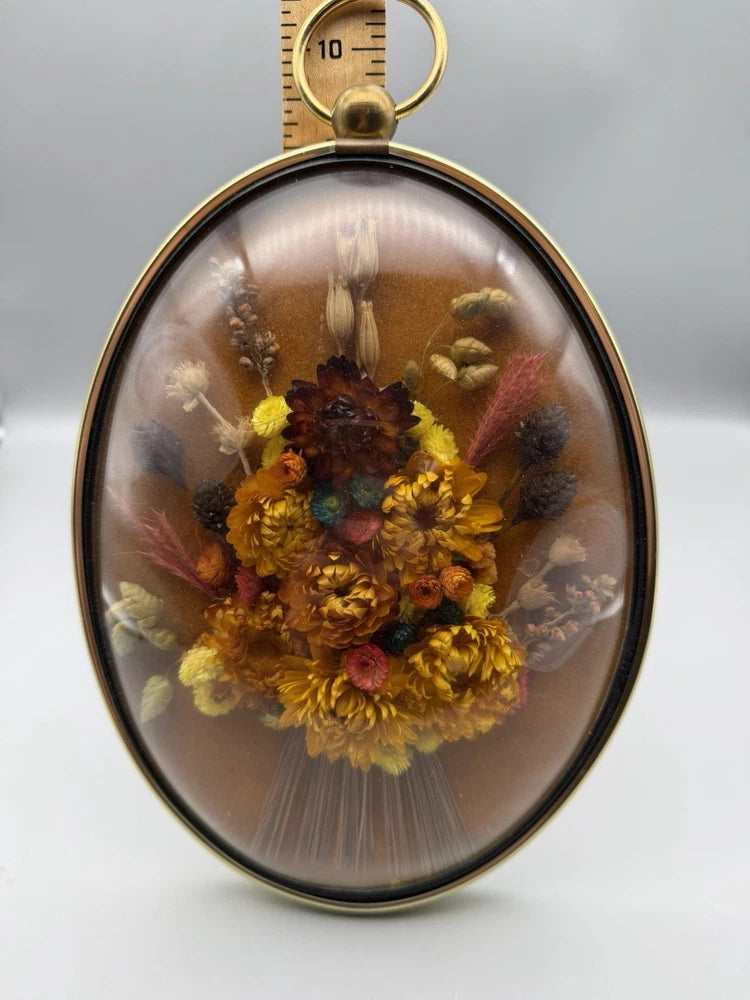 Domed glass oval wall hanging with encased dried yellow and brown flowers