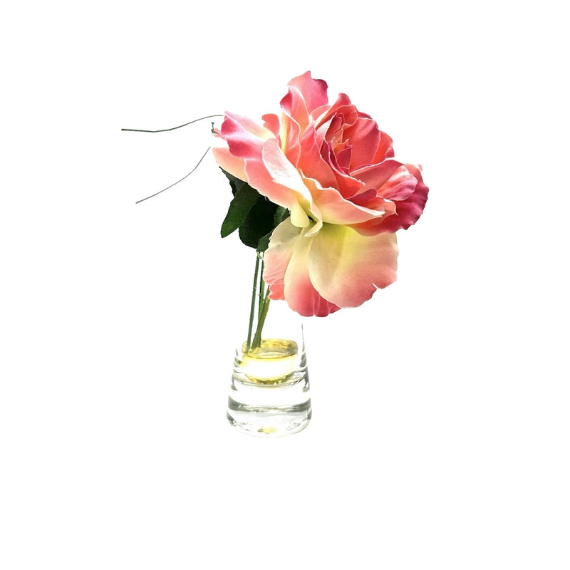 Artificial pink peony bouquet with green leaves in a small clear vase