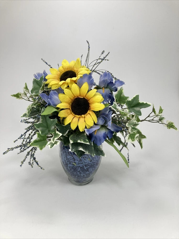 Silk artificial sunflower and blue flower bouquet in blue glass vase, with green leaves