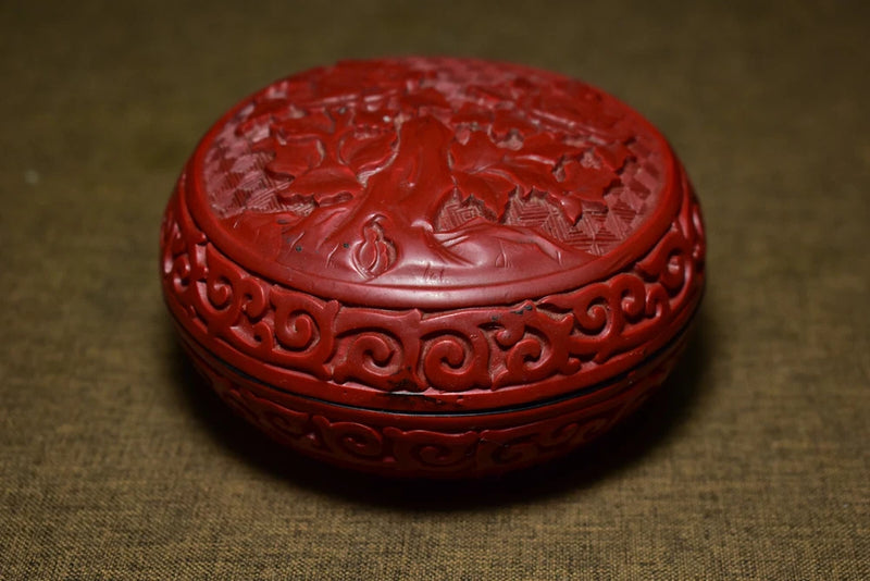 Red lacquer round jewelry box with carved peony lid and ornate scrollwork edges