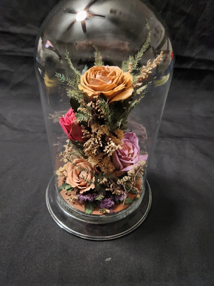 Glass dome cloche with dried roses and wildflowers in orange, pink, and purple