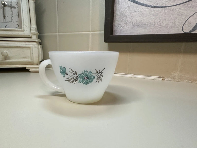 Vintage white tea cup with blue-green floral pattern and curved handle