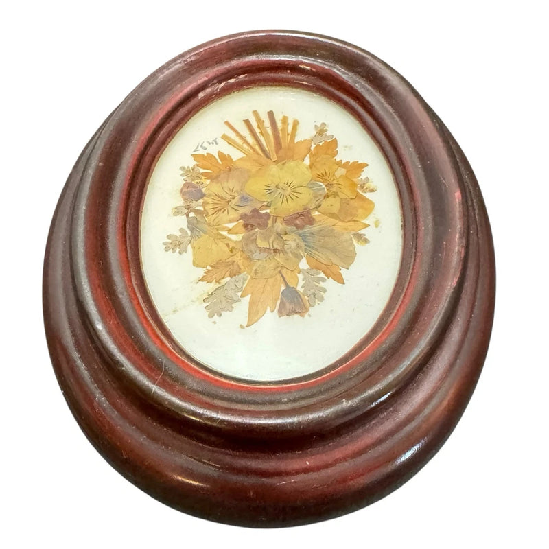 Oval brown wooden frame with pressed dried yellow flowers in center
