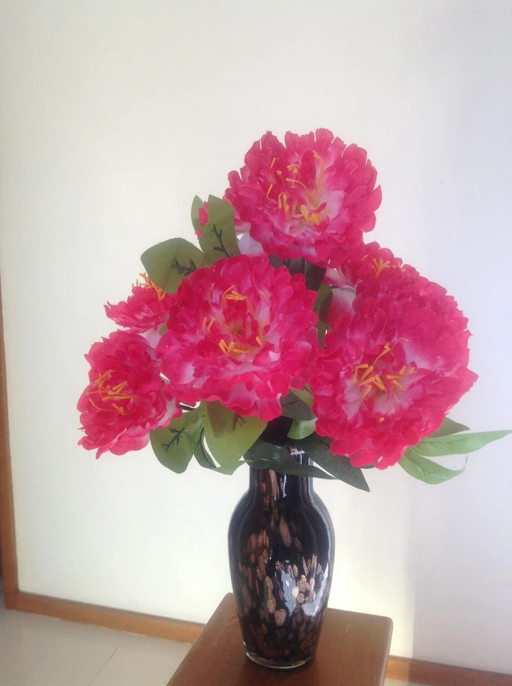 Artificial silk peony flowers in a dark vase, bright pink blooms with green leaves