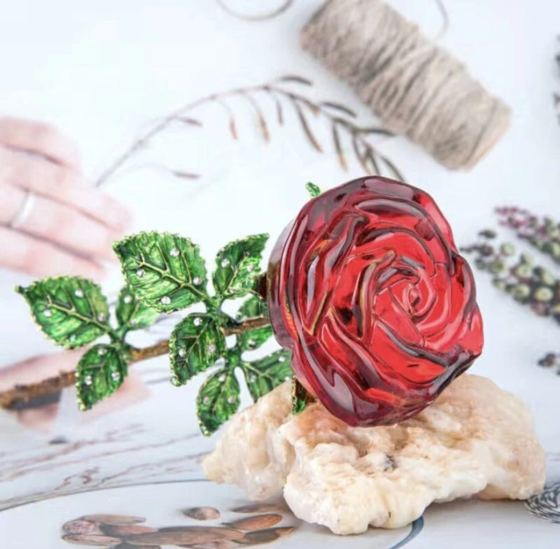 Red crystal rose with green leaf accents and gold-toned stem on a stone base