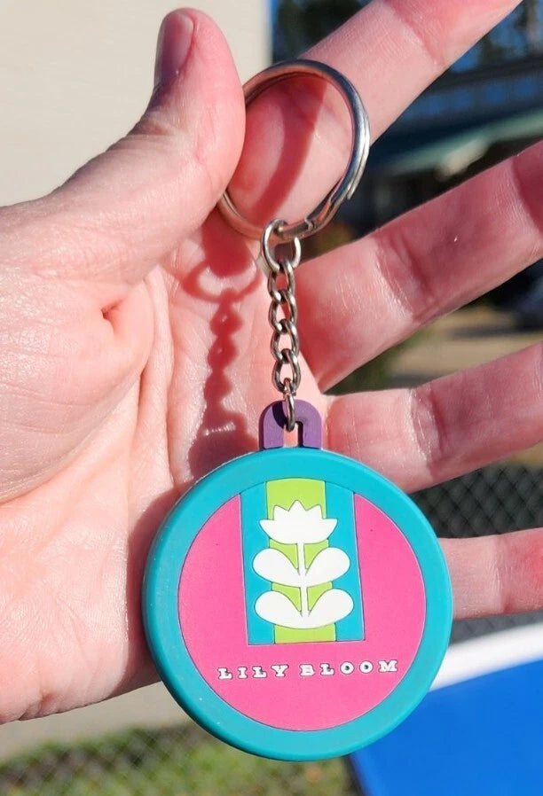Lily Bloom flower keychain charm with teal rim, pink-blue panel, and white flower logo