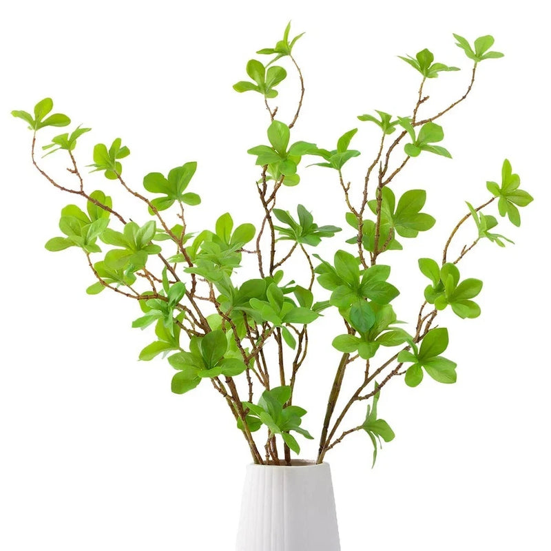 Artificial greenery stems with small green leaves on brown branches in a white vase