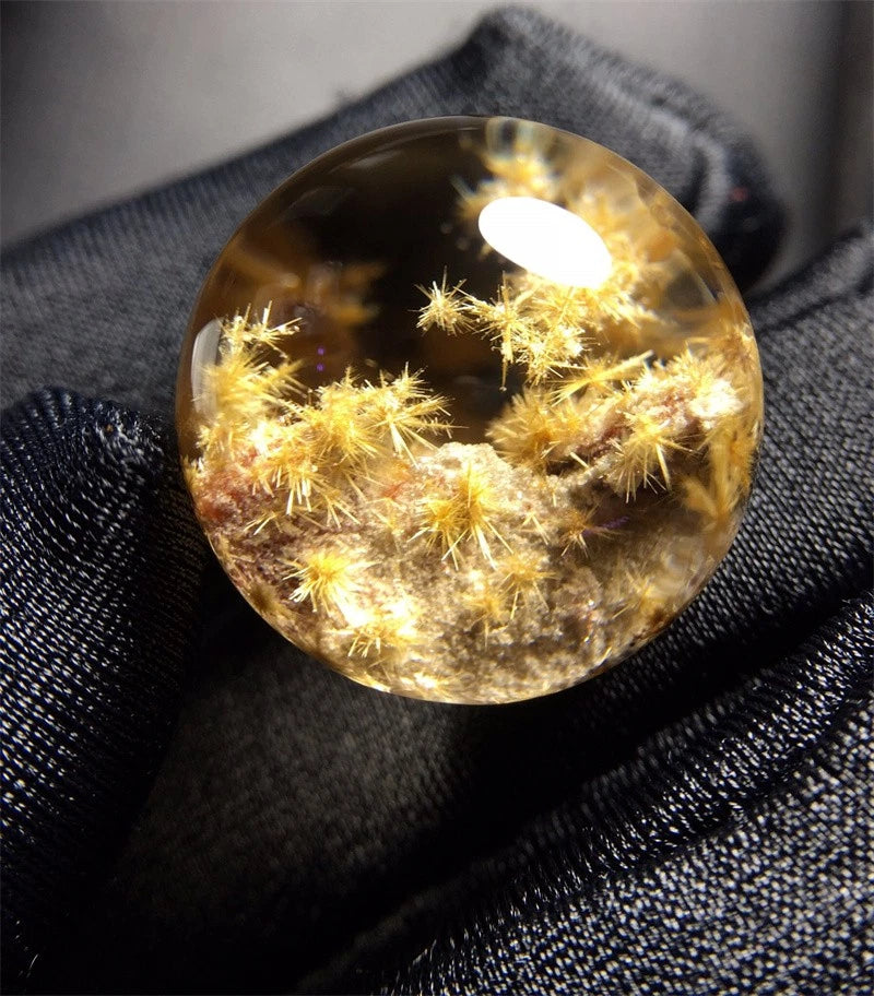 Natural quartz crystal ball with golden dandelion-like starburst speckles inside